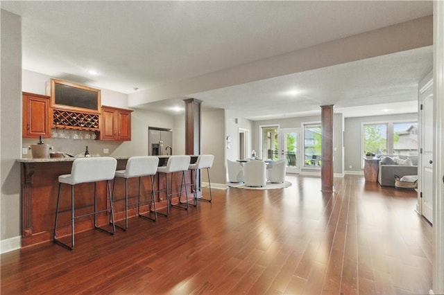 kitchen featuring stainless steel fridge, a kitchen breakfast bar, a peninsula, open floor plan, and ornate columns
