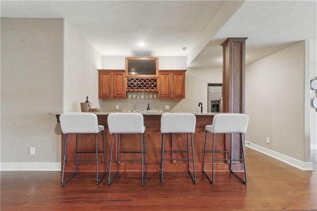 bar featuring baseboards, wet bar, and dark wood-style flooring