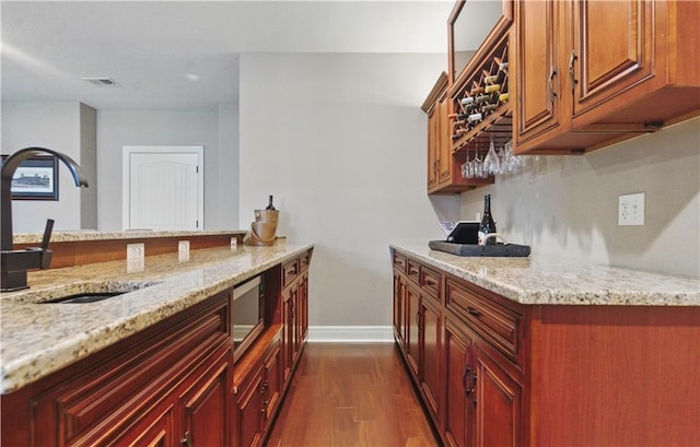 bar featuring a sink, stainless steel microwave, baseboards, indoor bar, and dark wood-style floors