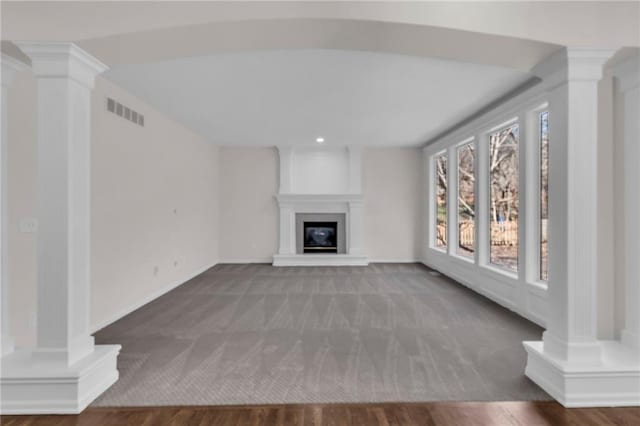 unfurnished living room with visible vents, a fireplace, ornate columns, and wood finished floors