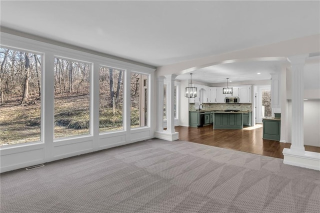 unfurnished living room with dark colored carpet, recessed lighting, visible vents, a chandelier, and ornate columns