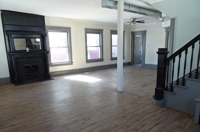 unfurnished living room featuring dark wood-style floors, stairway, baseboards, and crown molding