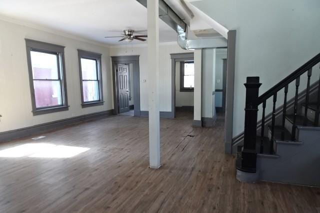 unfurnished living room with ceiling fan, wood finished floors, baseboards, ornamental molding, and stairway