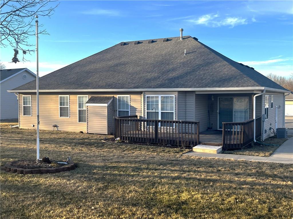 rear view of property with a shingled roof, a lawn, and a deck