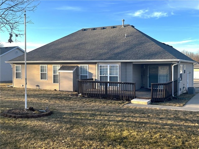 rear view of property with a shingled roof, a lawn, and a deck