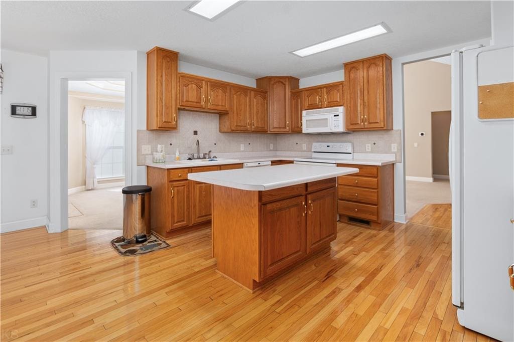 kitchen with tasteful backsplash, light wood-type flooring, white appliances, and light countertops