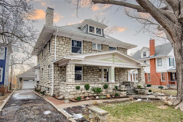 american foursquare style home featuring an outbuilding, aphalt driveway, stone siding, a garage, and a chimney