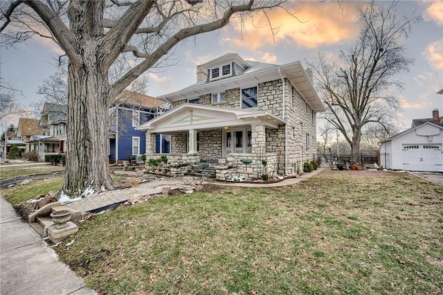 traditional style home with a front yard, an outbuilding, covered porch, stone siding, and a detached garage