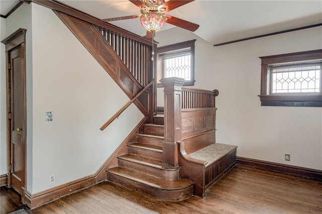 staircase featuring baseboards, wood finished floors, a ceiling fan, and crown molding