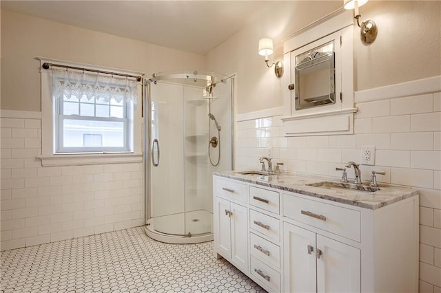 full bath featuring tile walls, double vanity, a stall shower, and a sink