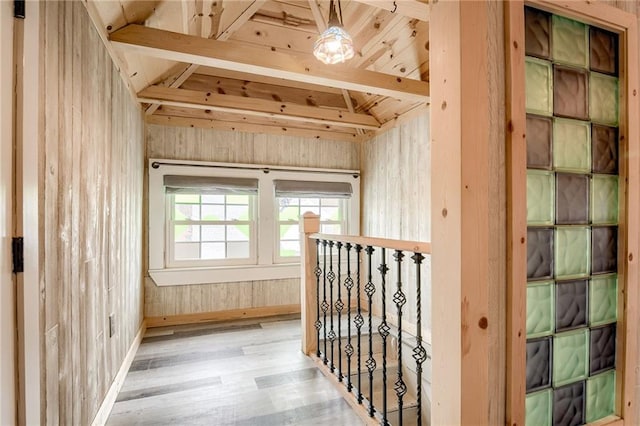 corridor featuring an upstairs landing, wooden walls, lofted ceiling, and wood finished floors