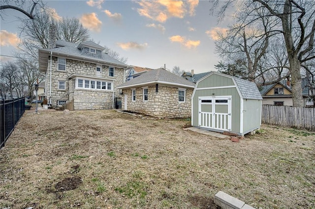 rear view of house featuring an outbuilding, stone siding, a shed, and a fenced backyard