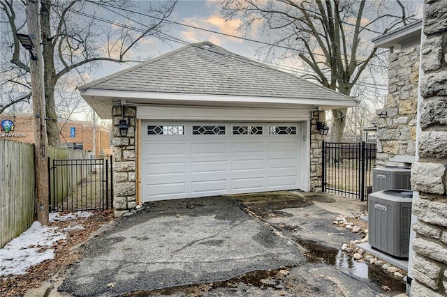 garage at dusk featuring a gate, central AC, and fence