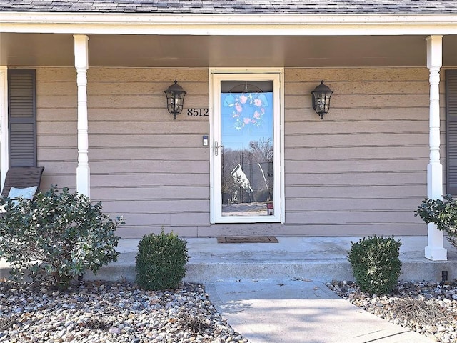 view of exterior entry with covered porch and a shingled roof