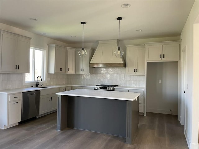 kitchen featuring stove, a center island, custom exhaust hood, stainless steel dishwasher, and a sink