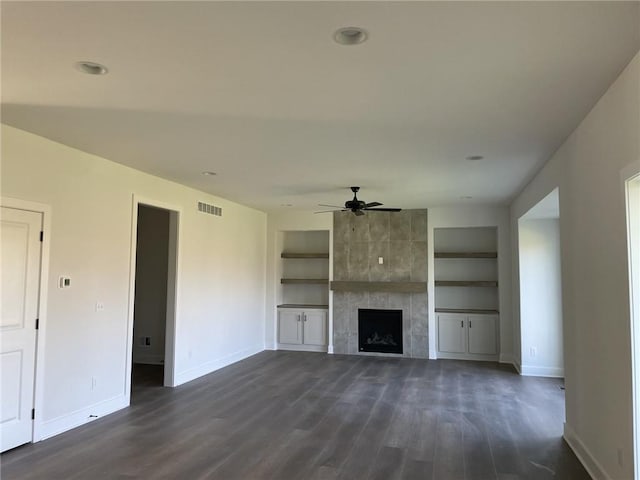 unfurnished living room with visible vents, built in features, baseboards, dark wood-style floors, and a tiled fireplace