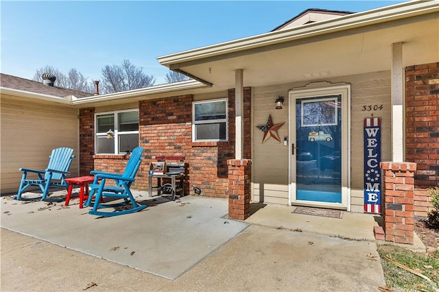 view of exterior entry featuring a porch and brick siding