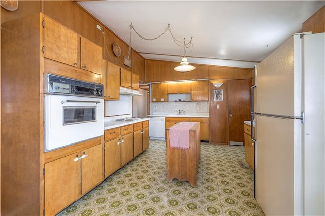 kitchen with white appliances, vaulted ceiling, light countertops, light floors, and brown cabinetry