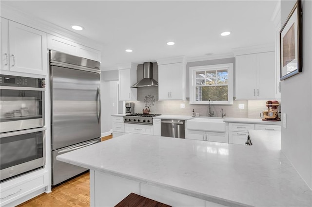 kitchen featuring backsplash, appliances with stainless steel finishes, white cabinets, a sink, and wall chimney range hood