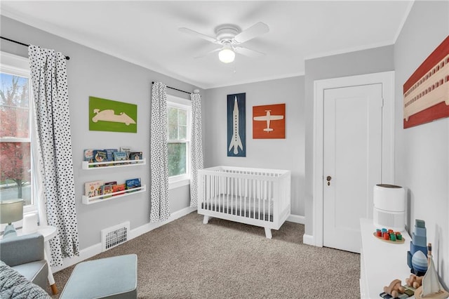 carpeted bedroom with crown molding, visible vents, a ceiling fan, a crib, and baseboards