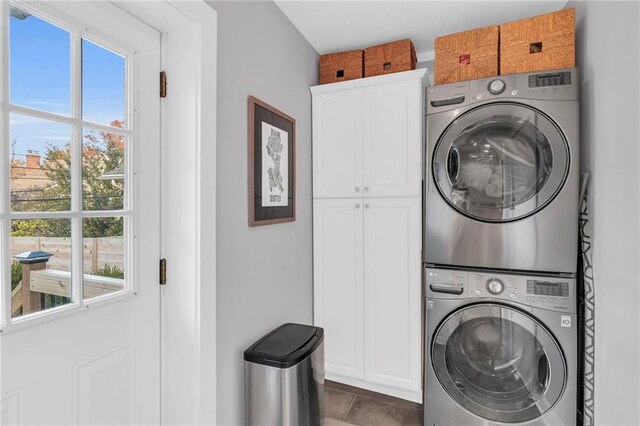 clothes washing area featuring stacked washer and dryer, cabinet space, and a healthy amount of sunlight