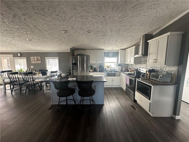 kitchen with wall chimney range hood, dark wood-type flooring, stainless steel appliances, and a sink