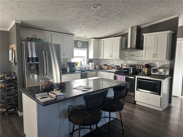 kitchen featuring wall chimney exhaust hood, appliances with stainless steel finishes, dark wood finished floors, and ornamental molding