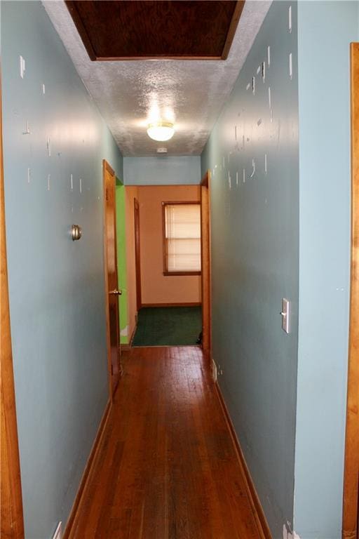 corridor with a textured ceiling, wood finished floors, and baseboards