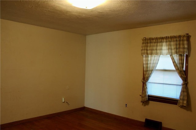 unfurnished room with a textured ceiling, wood finished floors, visible vents, and baseboards