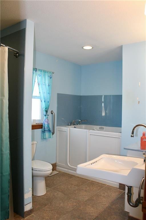 bathroom with a garden tub, a sink, and toilet