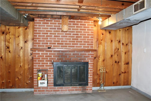 room details with wood walls, concrete floors, a fireplace, visible vents, and baseboards