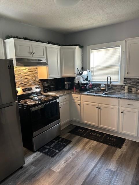 kitchen with under cabinet range hood, freestanding refrigerator, electric stove, white cabinetry, and a sink