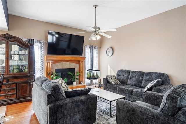 living room featuring light wood-style floors, ceiling fan, and a tile fireplace