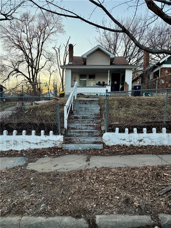 bungalow-style home featuring a fenced front yard, covered porch, and a chimney