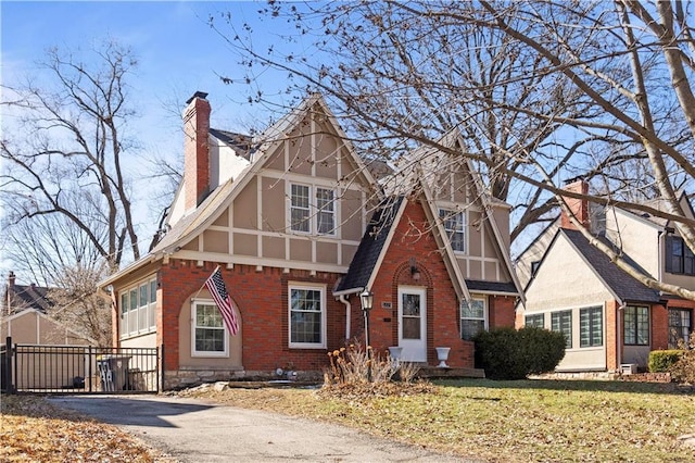 english style home with a front yard, fence, driveway, a chimney, and brick siding