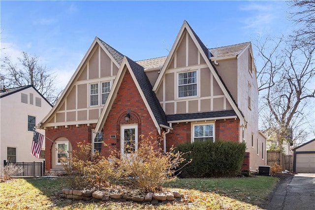 english style home featuring brick siding, fence, central AC unit, stucco siding, and an outbuilding