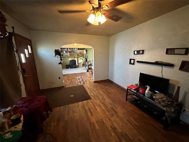 living area with arched walkways, ceiling fan, wood finished floors, and baseboards