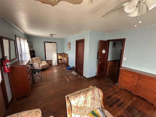 living area featuring baseboards, dark wood finished floors, and a ceiling fan