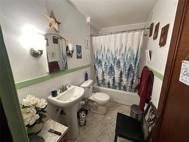 bathroom with wainscoting, shower / bath combination with curtain, and toilet