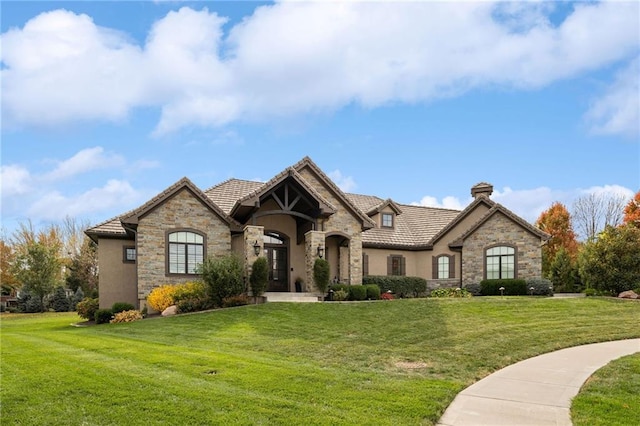 french country style house with stone siding, a front lawn, a tile roof, and stucco siding