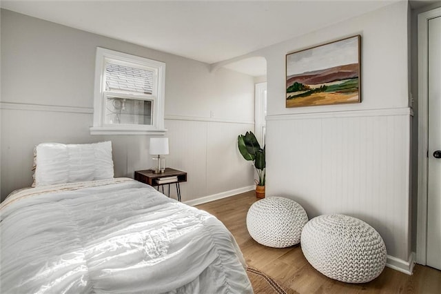 bedroom with a wainscoted wall and wood finished floors