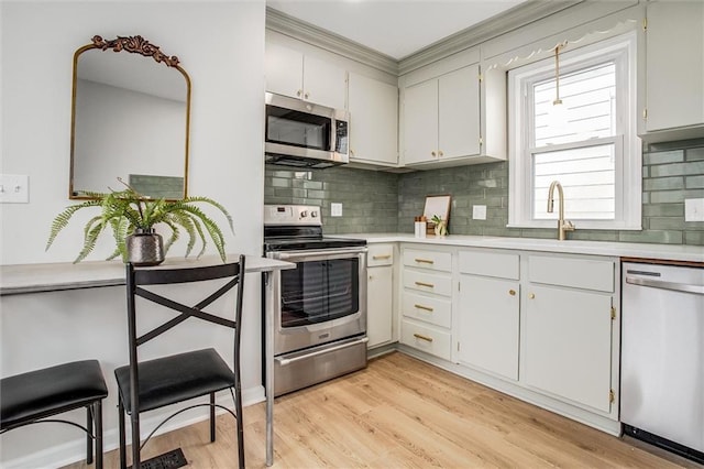 kitchen with light wood-style flooring, stainless steel appliances, a sink, light countertops, and decorative backsplash