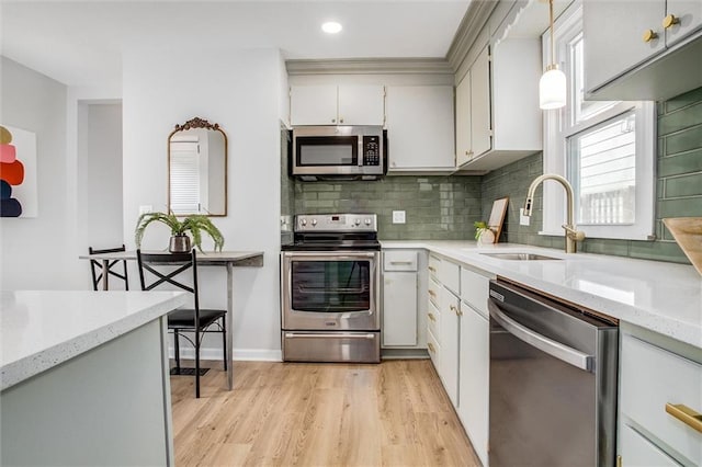 kitchen with light wood finished floors, appliances with stainless steel finishes, backsplash, and a sink