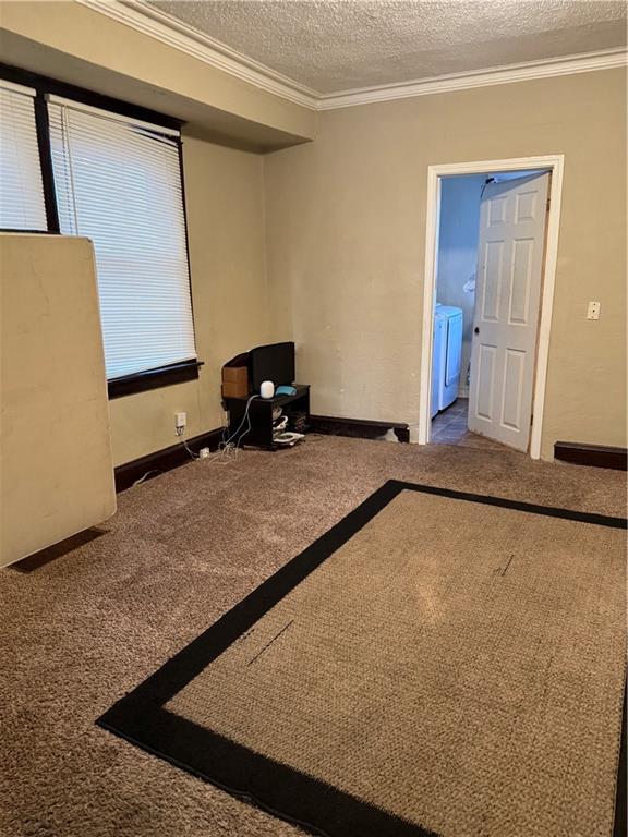 interior space featuring carpet flooring, ornamental molding, independent washer and dryer, and a textured ceiling