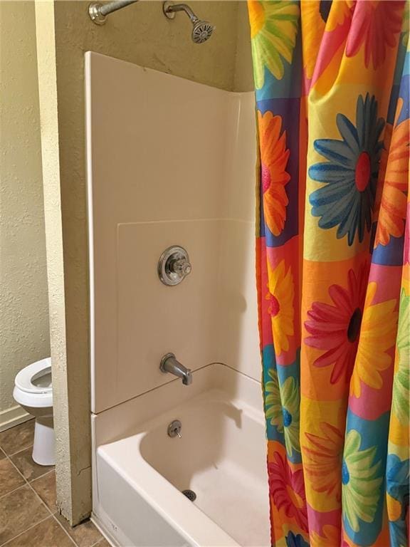 bathroom with tile patterned floors, toilet, shower / tub combo, and a textured wall