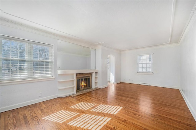 unfurnished living room with a fireplace with flush hearth, arched walkways, crown molding, and wood finished floors