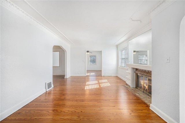 unfurnished living room featuring visible vents, arched walkways, a ceiling fan, a fireplace with flush hearth, and wood finished floors