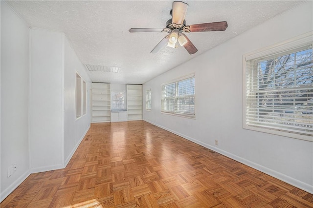 empty room featuring a textured ceiling, built in shelves, visible vents, and baseboards