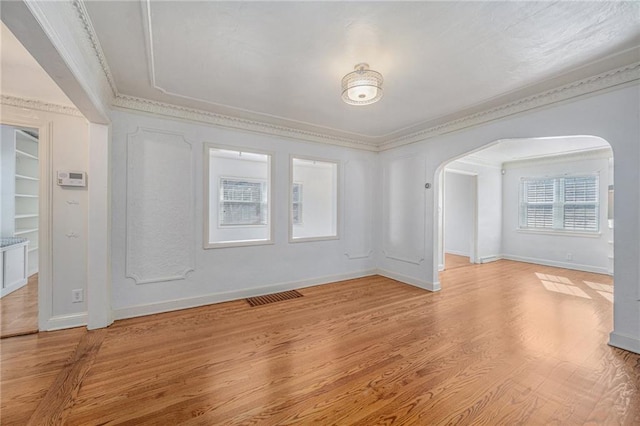 unfurnished room with light wood-type flooring, visible vents, arched walkways, and ornamental molding