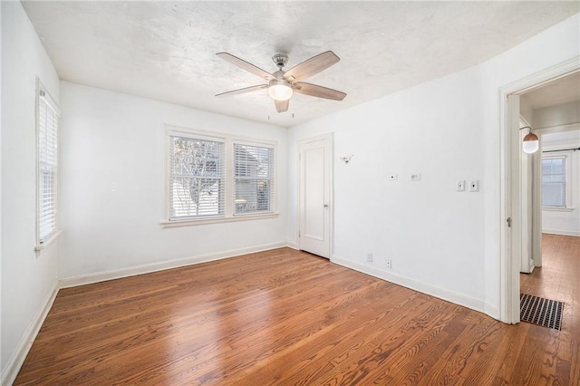 spare room with a healthy amount of sunlight, visible vents, baseboards, and wood finished floors